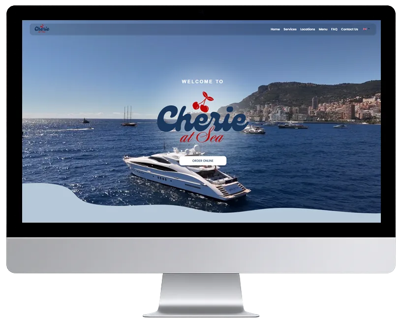 A silver flat-panel monitor showing a 2025 travel website: one full-bleed photograph of a yacht off a Mediterranean coast, a script logo and a single small call to action.